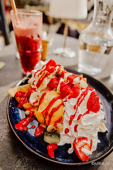 Ein Crêpe mit üppiger Sahne und Eis sowie ein Milchshake stehen auf dem Tisch.