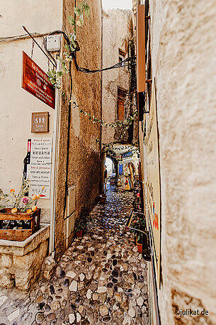 Eine enge Gasse mit bunten Kieselsteinen ziert den Weg.