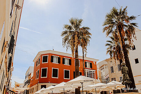 Eine schicke Plaza mit Palmen und Sonnenschirmen wird von britischer Architektur umringt.