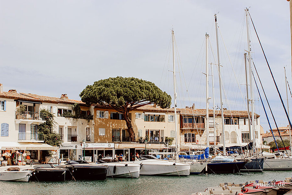 Seegelboote liegen auf dem ruhigen Gewässer vor den Cafés vor Anker.