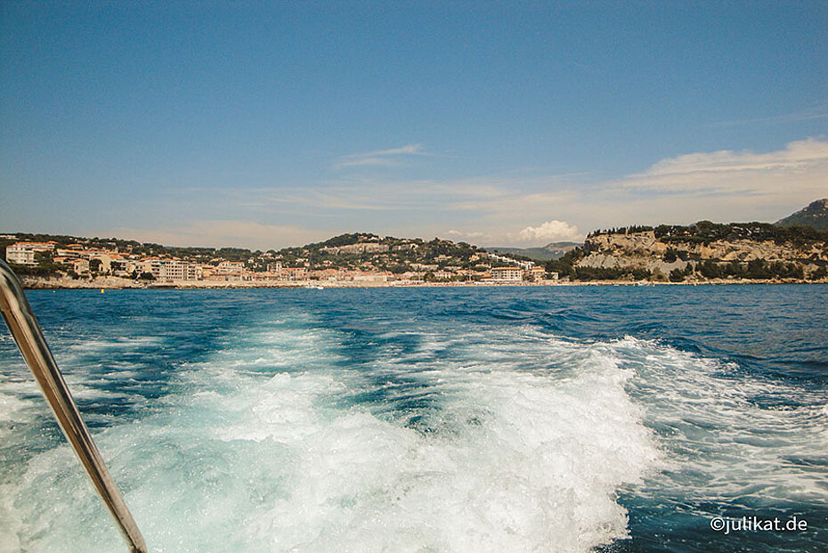 Blick vom Boot über weiße Gischt und Meeresküste