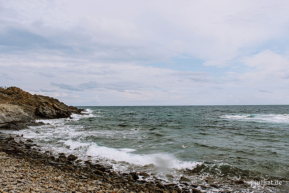 Eine raue meeresküste mit groben, dunklen Kieselstrand bestimmt den Norden Menorcas