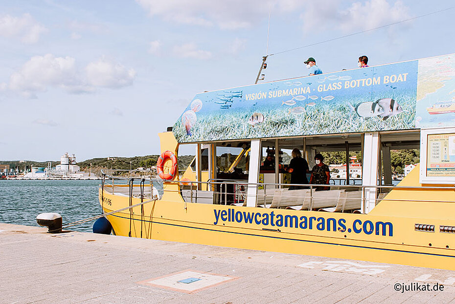 Ein gelber Katamaran mit bunter Aufschrift liegt am Pier vor Anker.